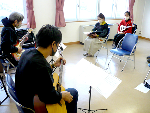 40代男性の生徒さんと講師のギター演奏とそれを聴く生徒さんの様子